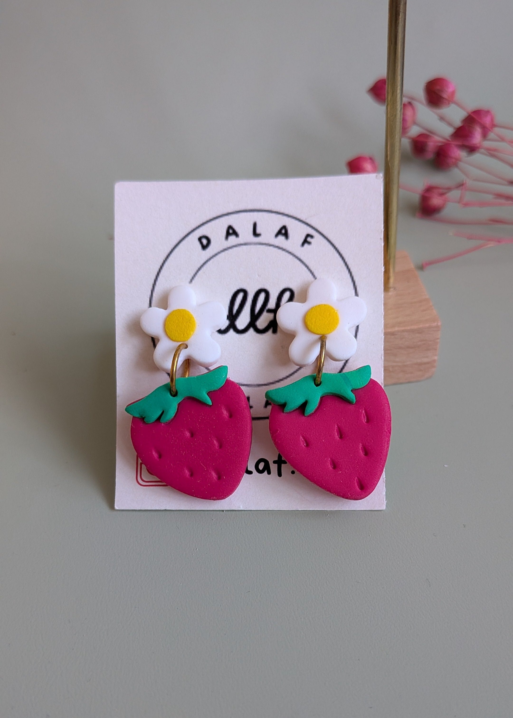 Pair of earrings shaped like strawberries and daisies on a branded card.